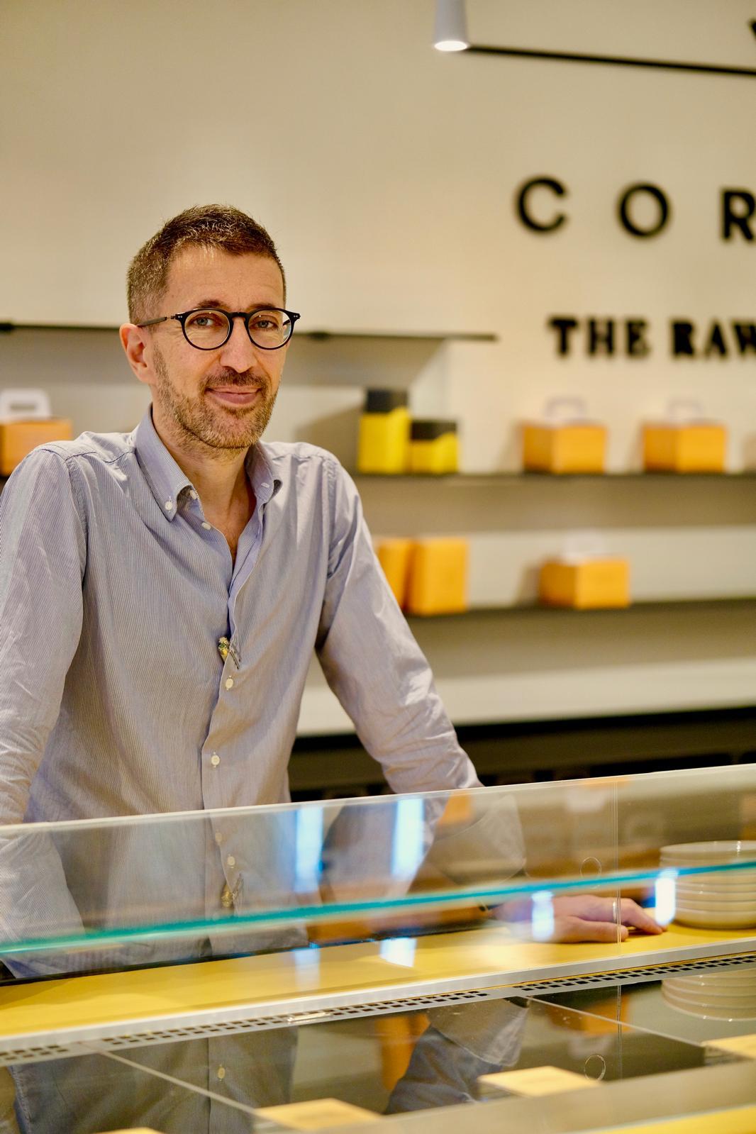 Interno Cortese The Raw Patisserie · committente davanti vetrina · scaffalature contenitori arancioni