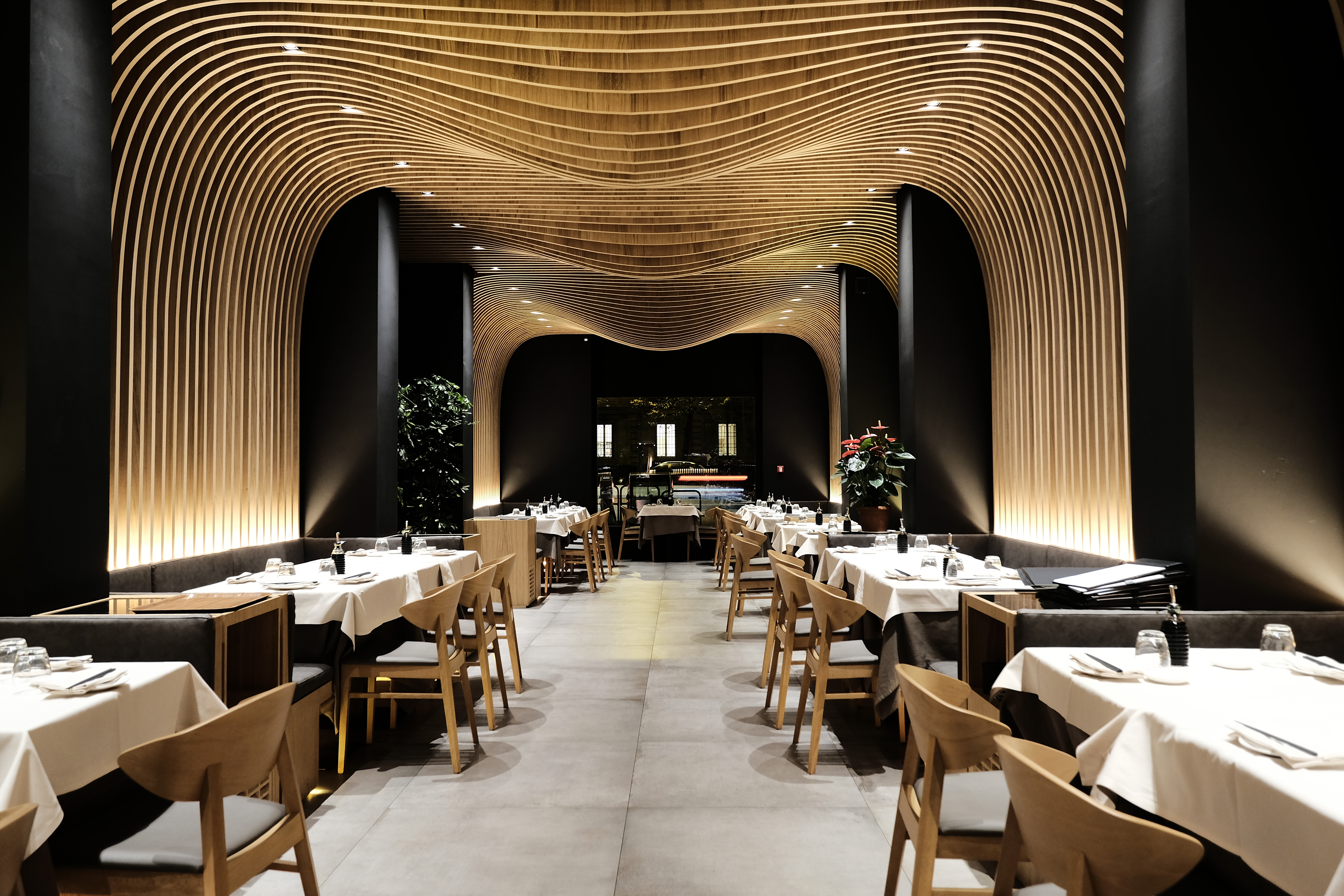 Sala da pranzo ristorante giapponese · soffitto in legno a doghe ondulate · tavoli apparecchiati ambiente scuro