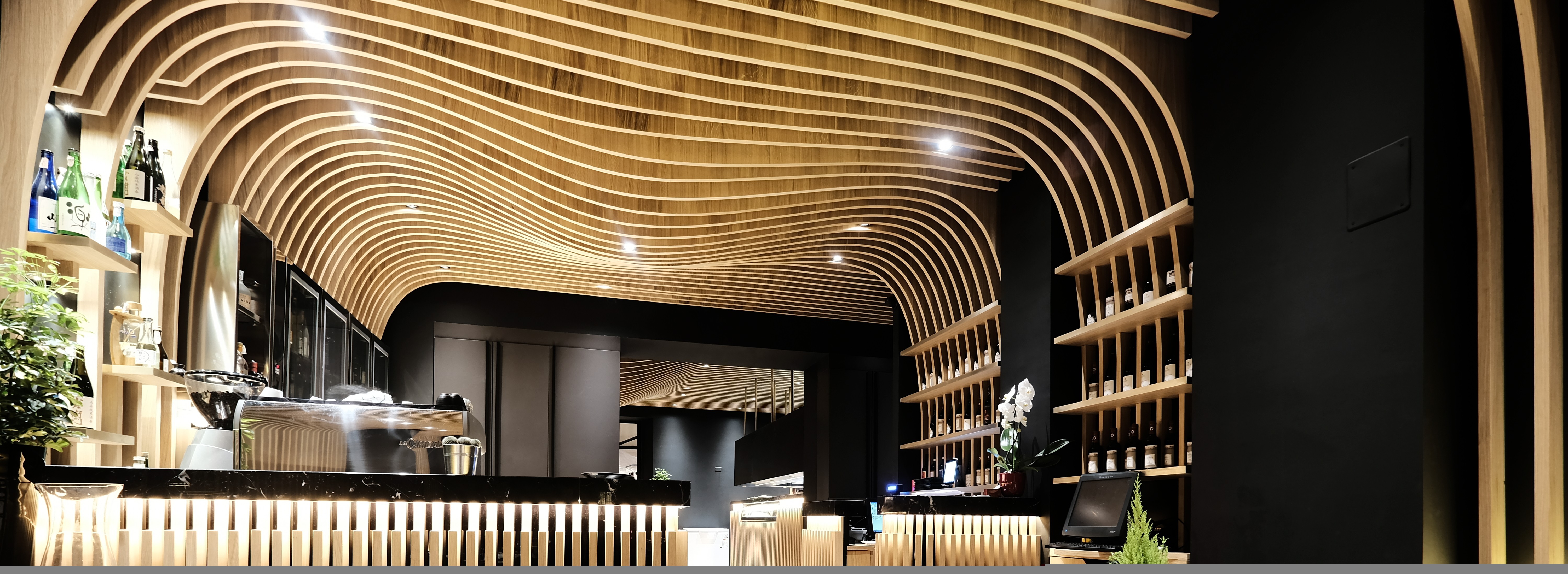 Bancone bar ristorante giapponese · soffitto legno ondulato · librerie cilindriche con piante e sake