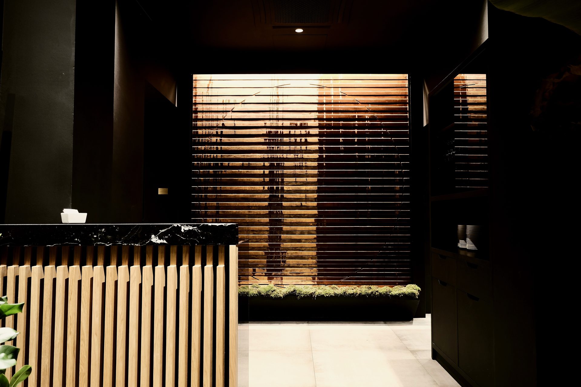 Aji Tei — parete in listoni di legno bronzo retroilluminata, soglia tra esterno e sala