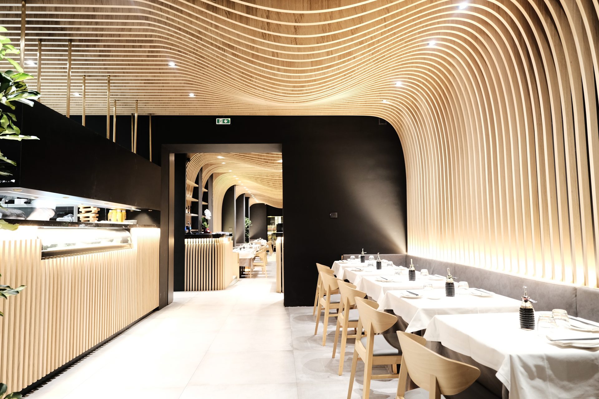 Aji Tei — sala ad arco con sushi counter a vista e tavoli apparecchiati