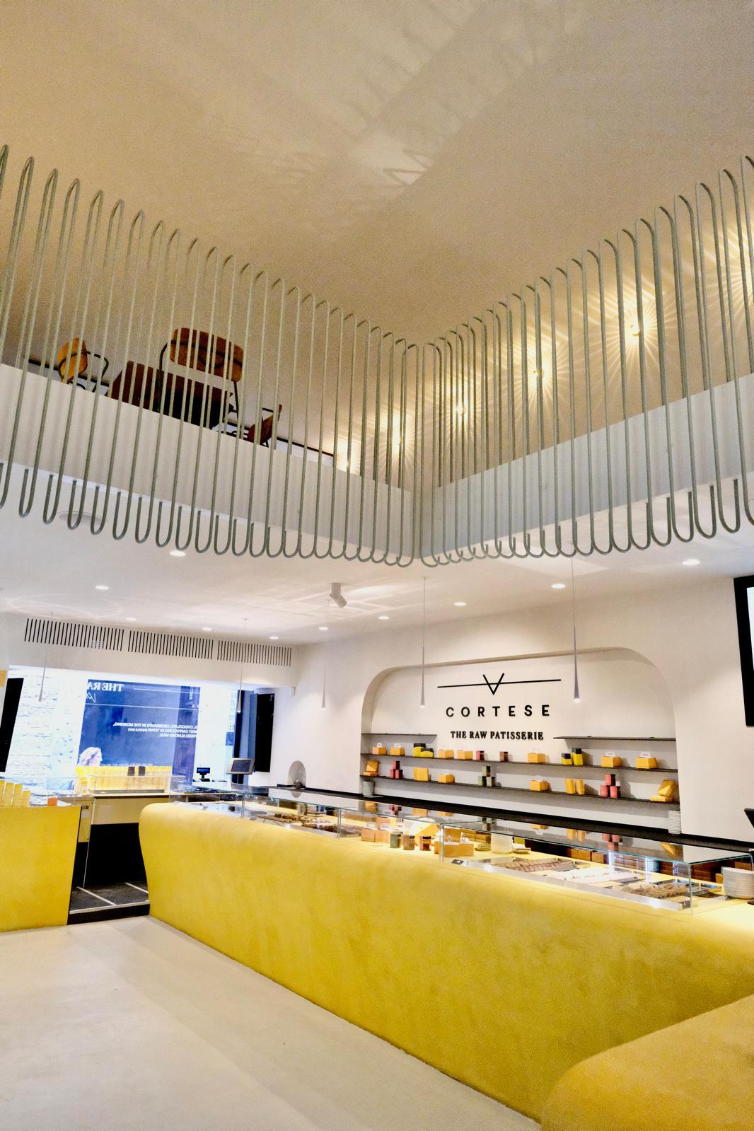 Cortese Caffè — struttura sage sospesa al soffitto, vista verticale con scritta CORTESE THE RAW PATISSERIE retro