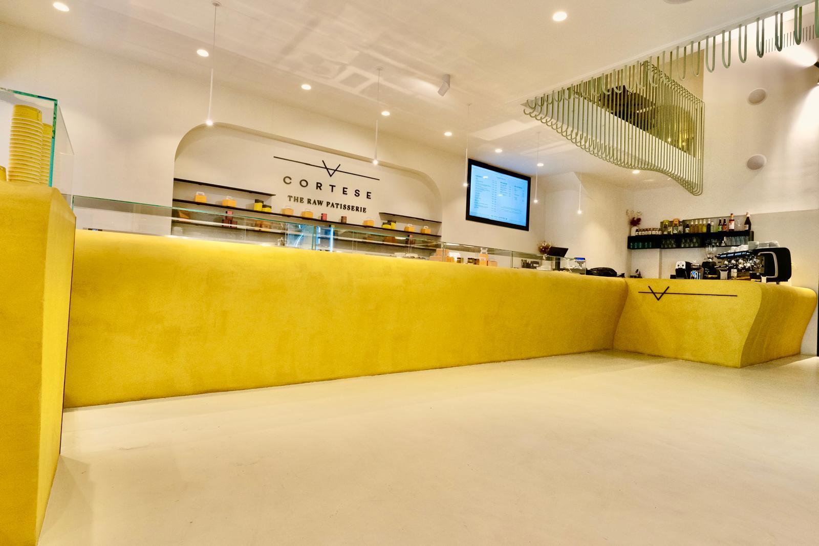 Cortese Caffè — vista d'insieme con banco continuo giallo, bancone bar e struttura sage sospesa al soffitto